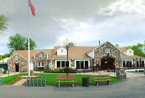 Stone building with US flag, green lawn, benches, and outdoor seating.