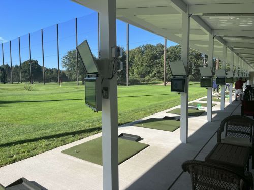 Golf driving range with white pillars, screens, green mats, and net barrier.