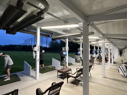 Golfers practicing at a covered driving range. Dusk setting, players hitting balls.
