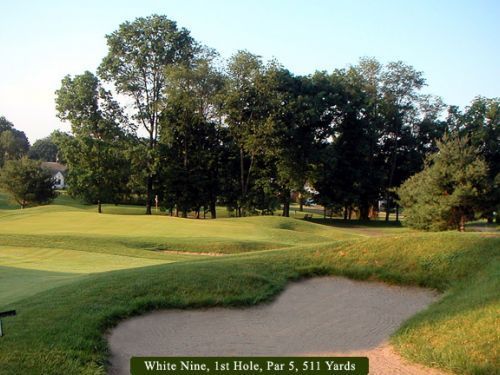 Golf course hole with sand trap, green fairway, and trees. White Nine, 1st Hole, Par 5, 511 Yards.