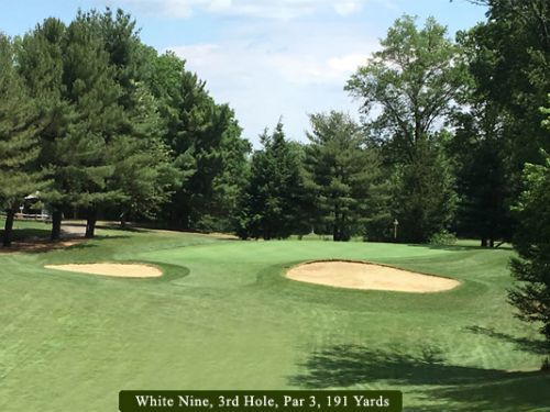 Golf course green with two sand traps, trees, and signage: 