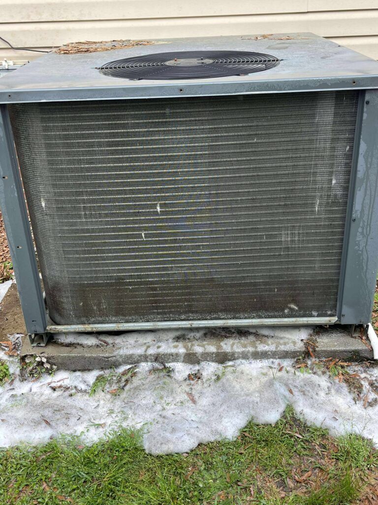 Exterior air conditioning unit, dirty coils, sits on a concrete pad near grass.
