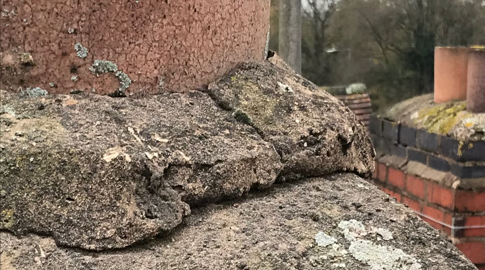 Close-up of weathered roof tiles on a chimney, with lichen and damage visible.