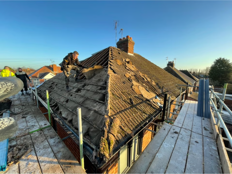 Workers repairing a damaged roof on a house, scaffolding surrounds the structure under a blue sky.