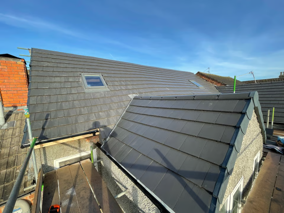 Newly tiled gray roof with skylight, scaffolding, and blue sky.