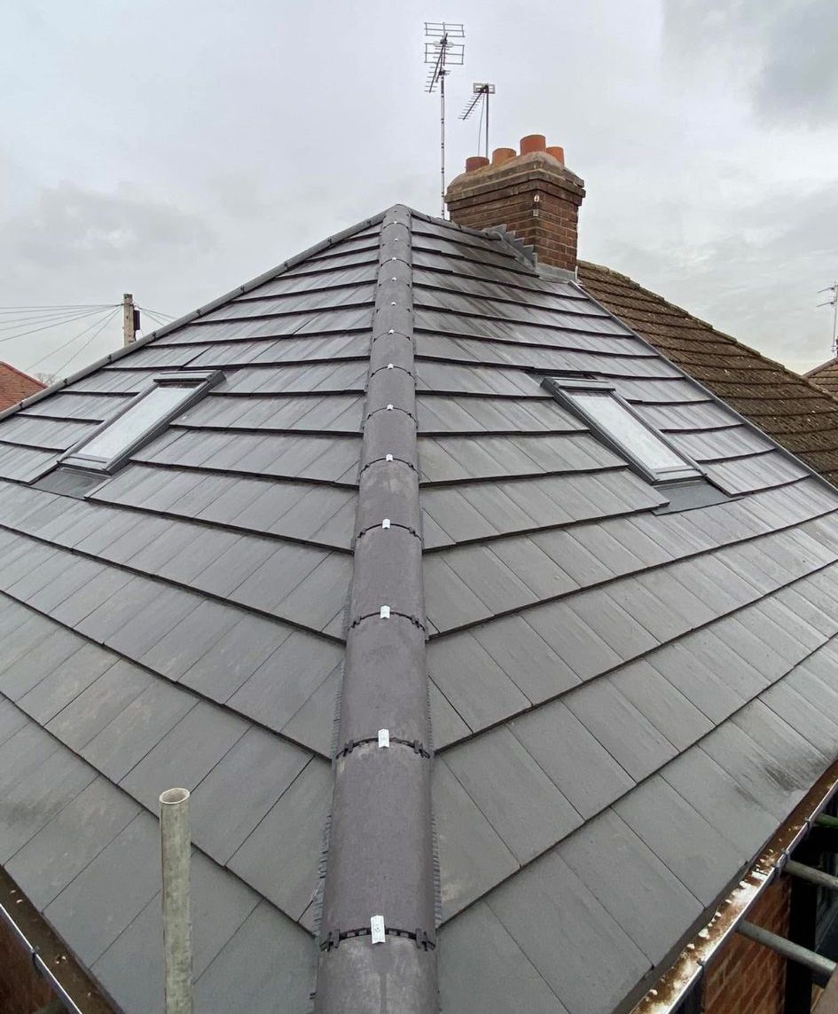 Grey tiled roof with skylights, ridge cap, and brick chimney against an overcast sky.