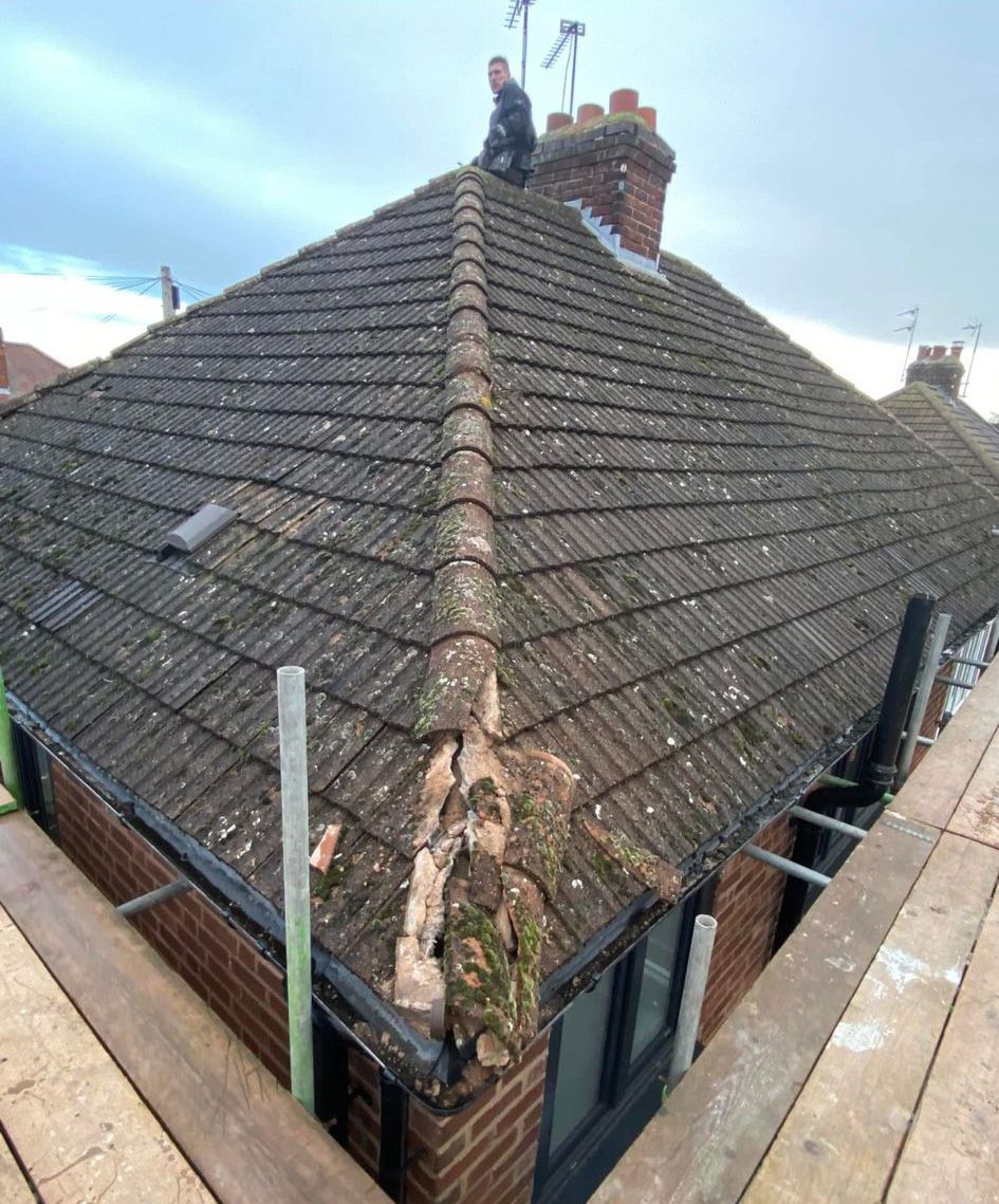Person on a roof repairing damage; scaffolding, brick house, weathered tiles, cloudy sky.