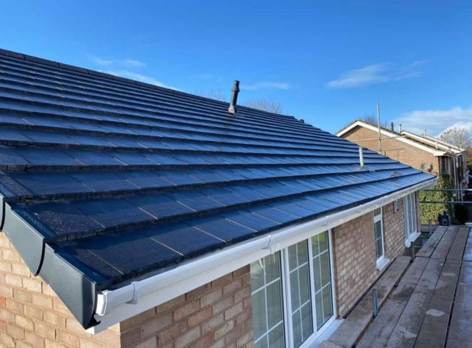 Dark blue tiled roof on a brick house with white gutters, under a blue sky.