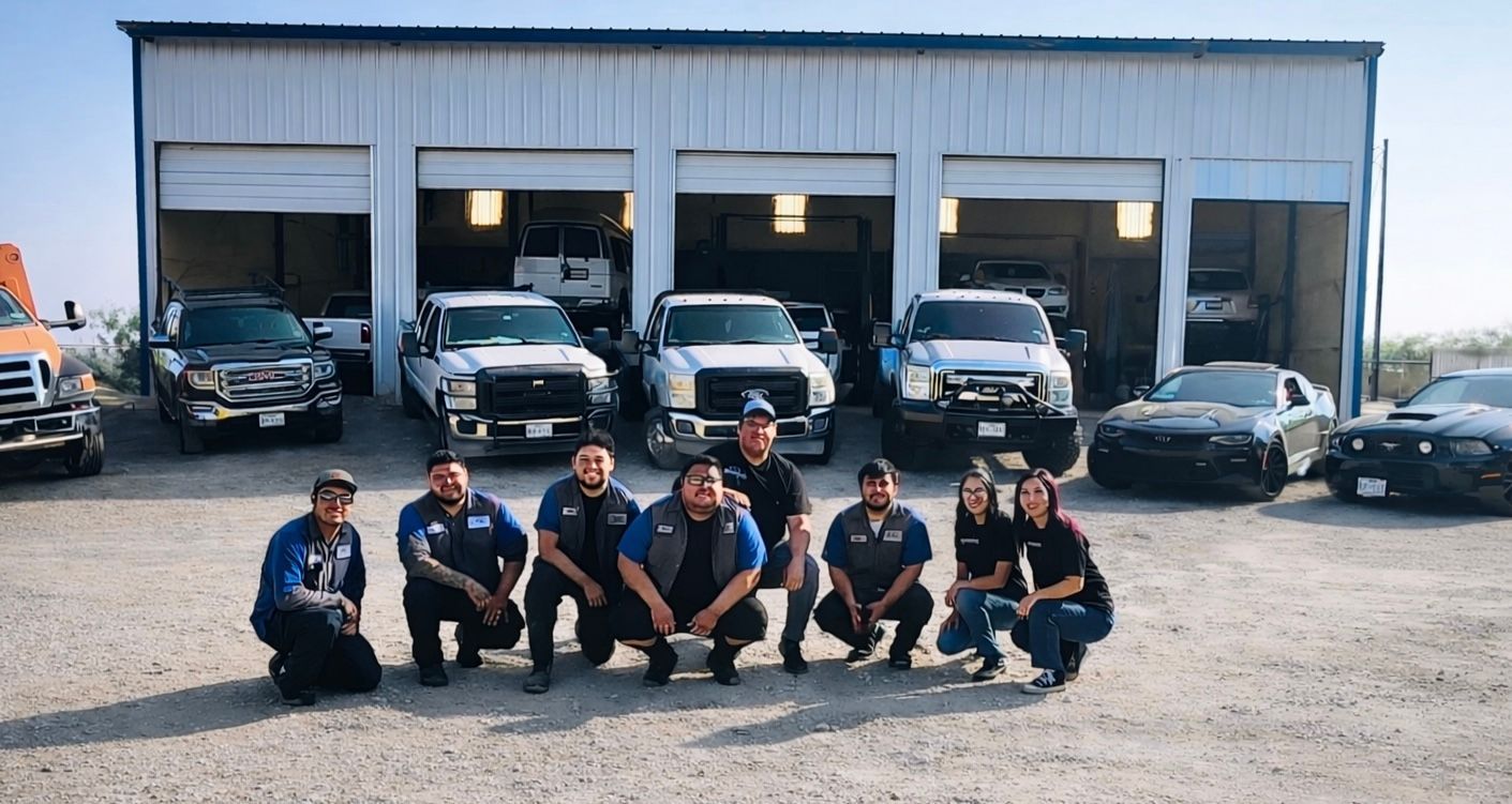 Mechanics pose with trucks in front of a garage. They are wearing blue shirts.