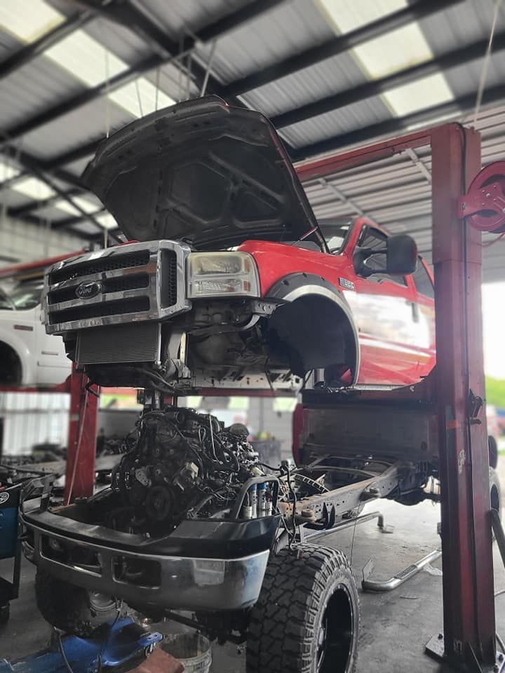 Red Ford pickup truck on a lift in a garage, engine removed, hood open.