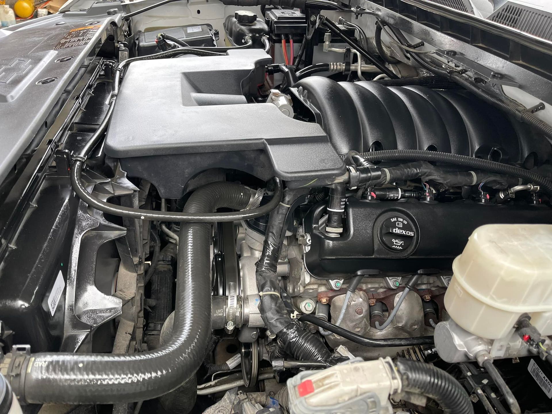 Clean engine bay of a vehicle; black engine, various hoses and wires, light-colored brake fluid reservoir.