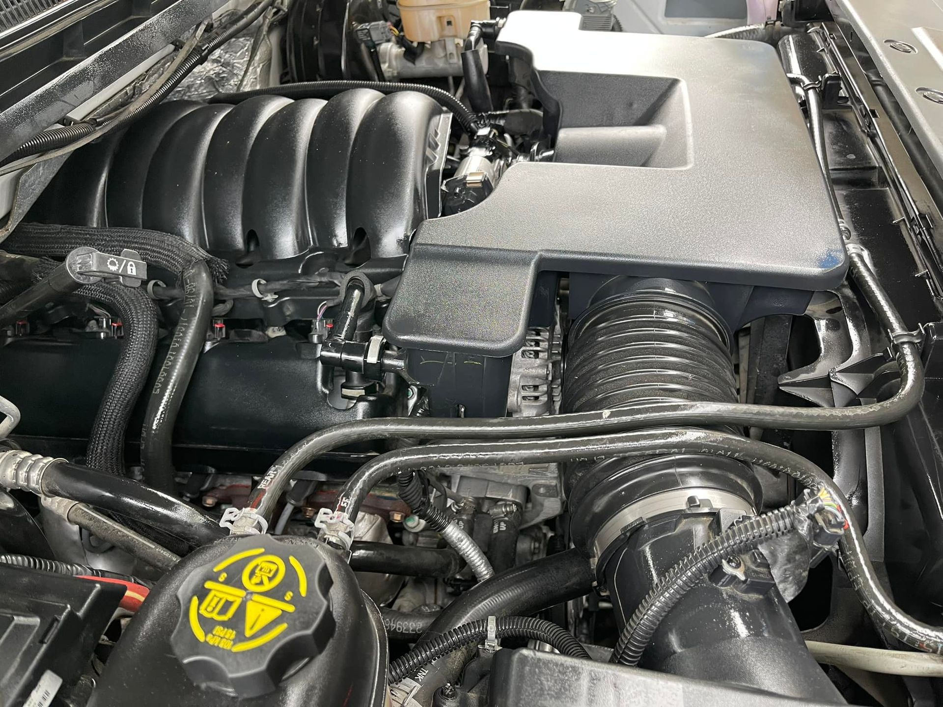 Engine bay of a vehicle, black engine components, intake, and hoses.