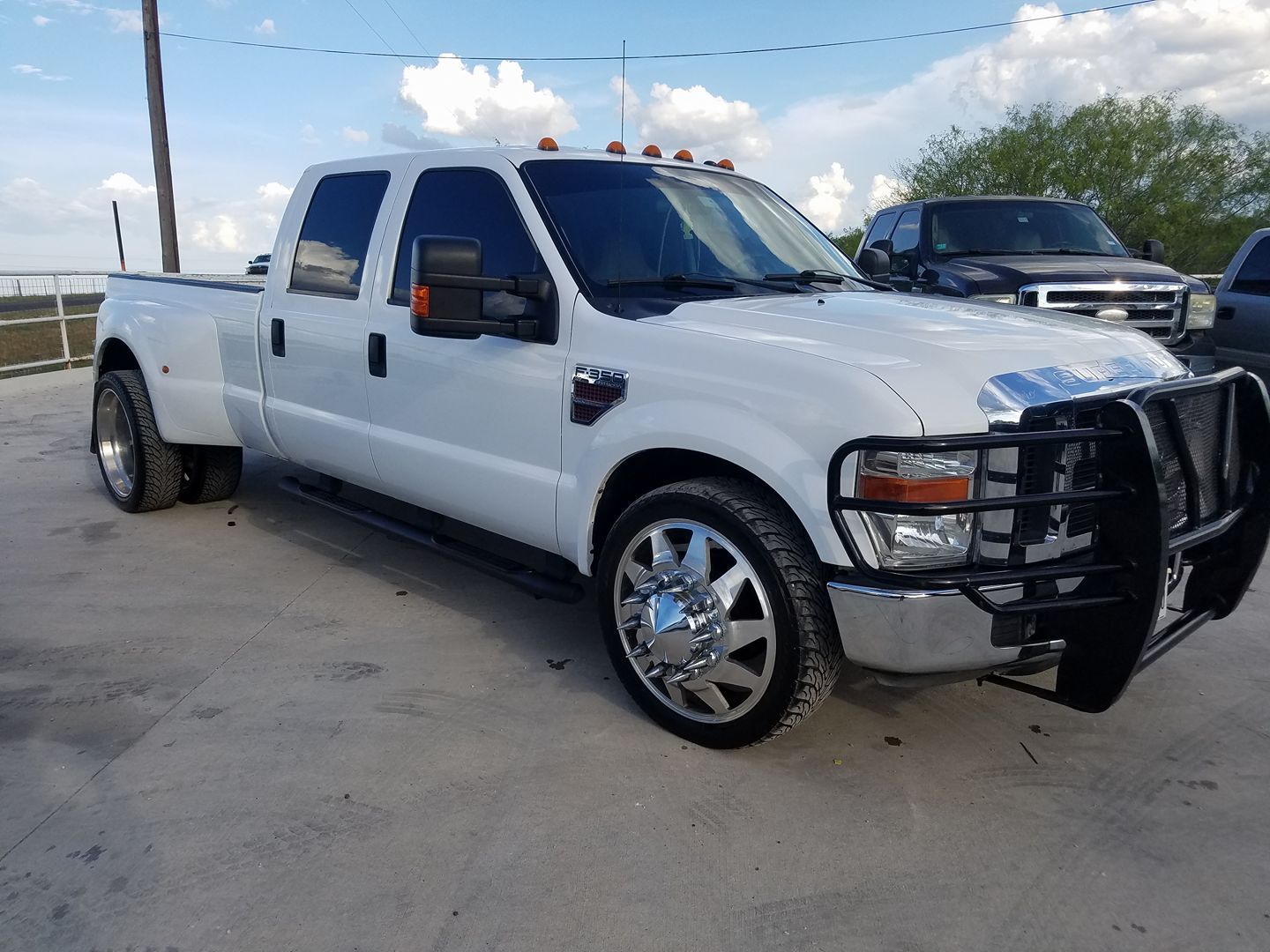 White Ford F-350 dually pickup truck with chrome wheels and a black brush guard parked outside on a cloudy day.