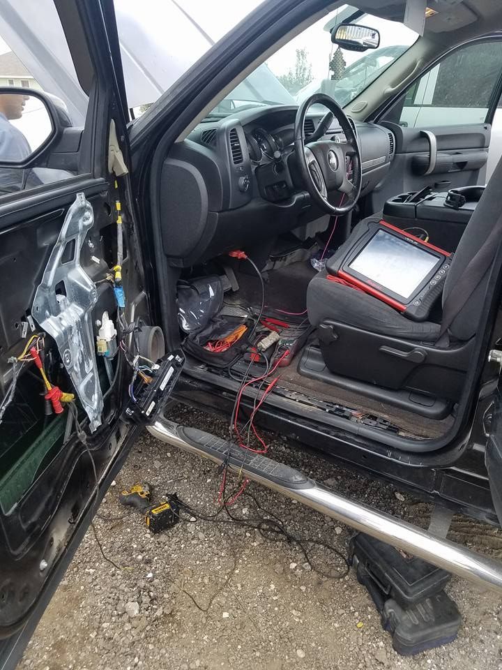 Interior of a black pickup truck with the door panel removed, diagnostic equipment on the seat.