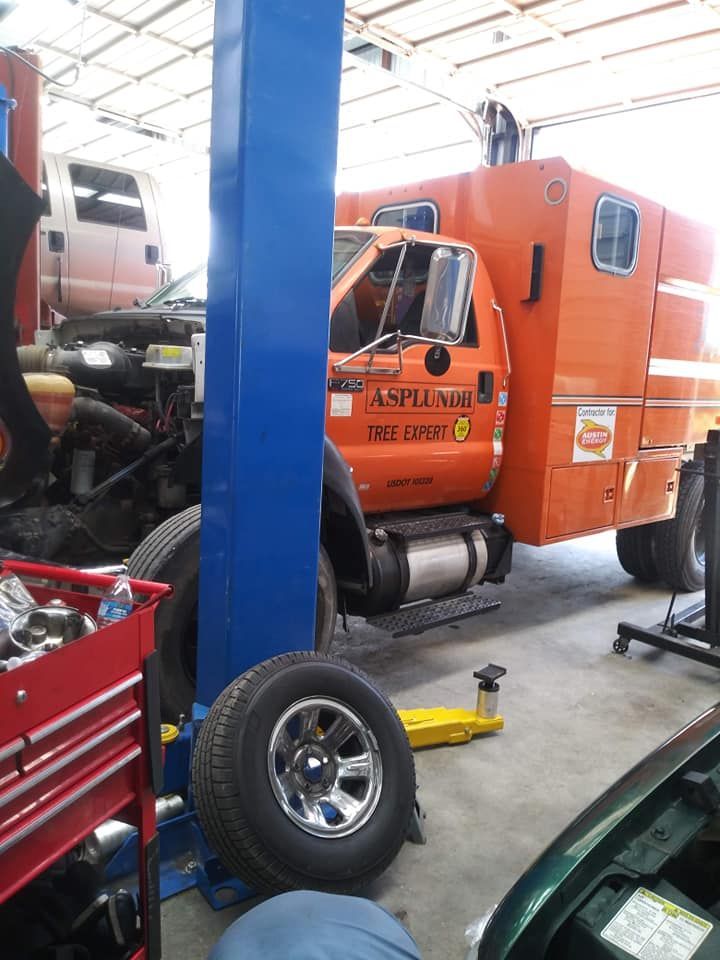 Orange truck being serviced in a garage, blue lift, removed tire on the floor.