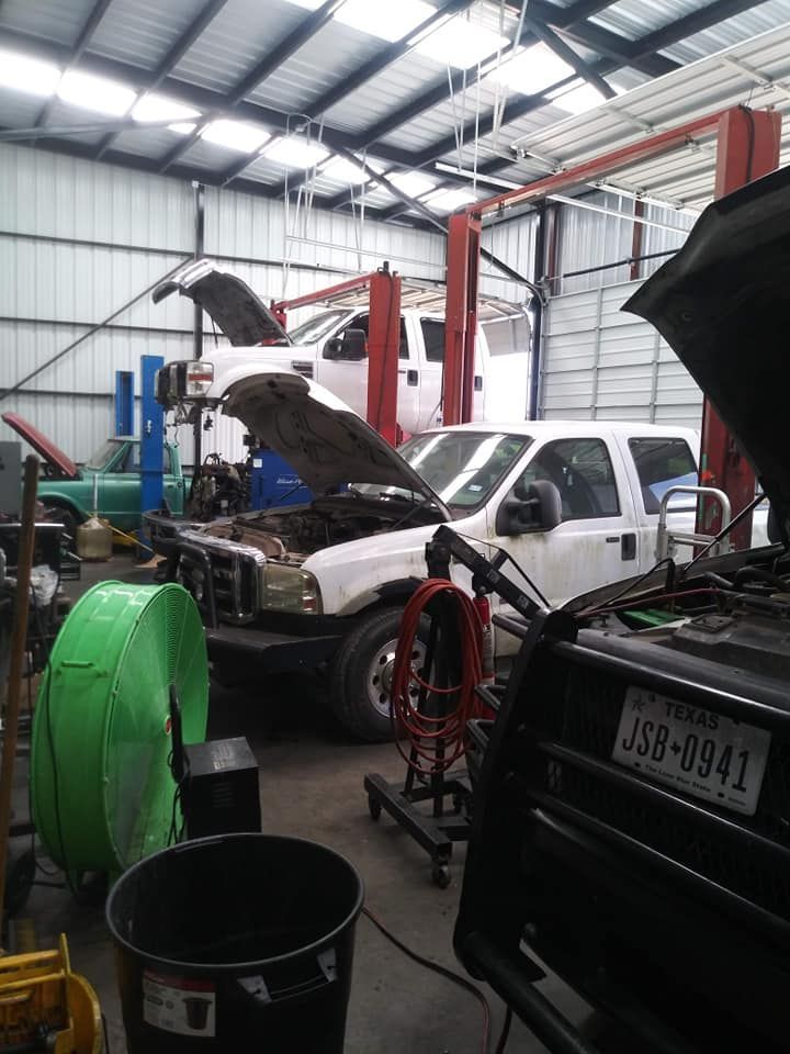 Vehicles being worked on inside a garage with car lifts. White and black cars with hoods up.