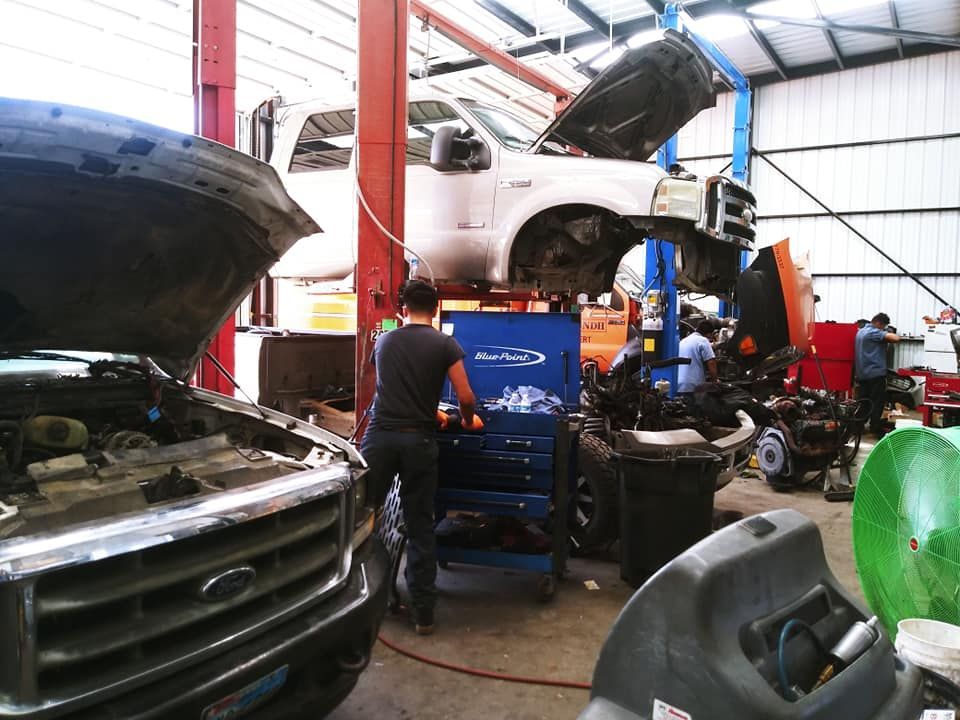 Mechanics working on trucks inside a repair shop. One truck is lifted, with hood and parts removed.