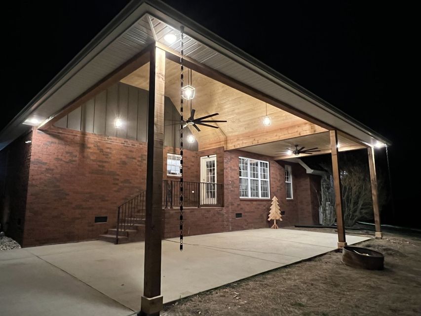 A brick house with a covered porch and a ceiling fan at night.