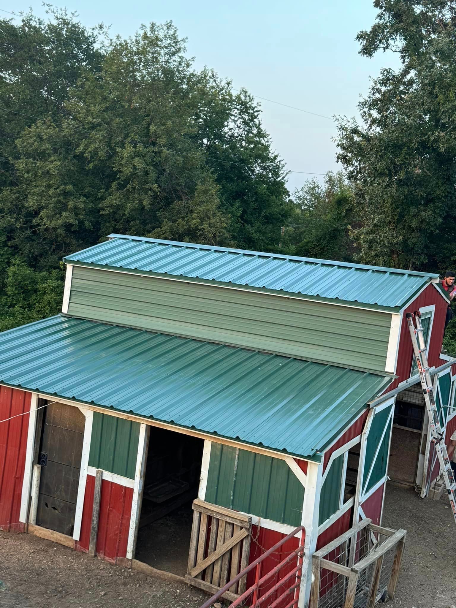 A red barn with a green roof is surrounded by trees.