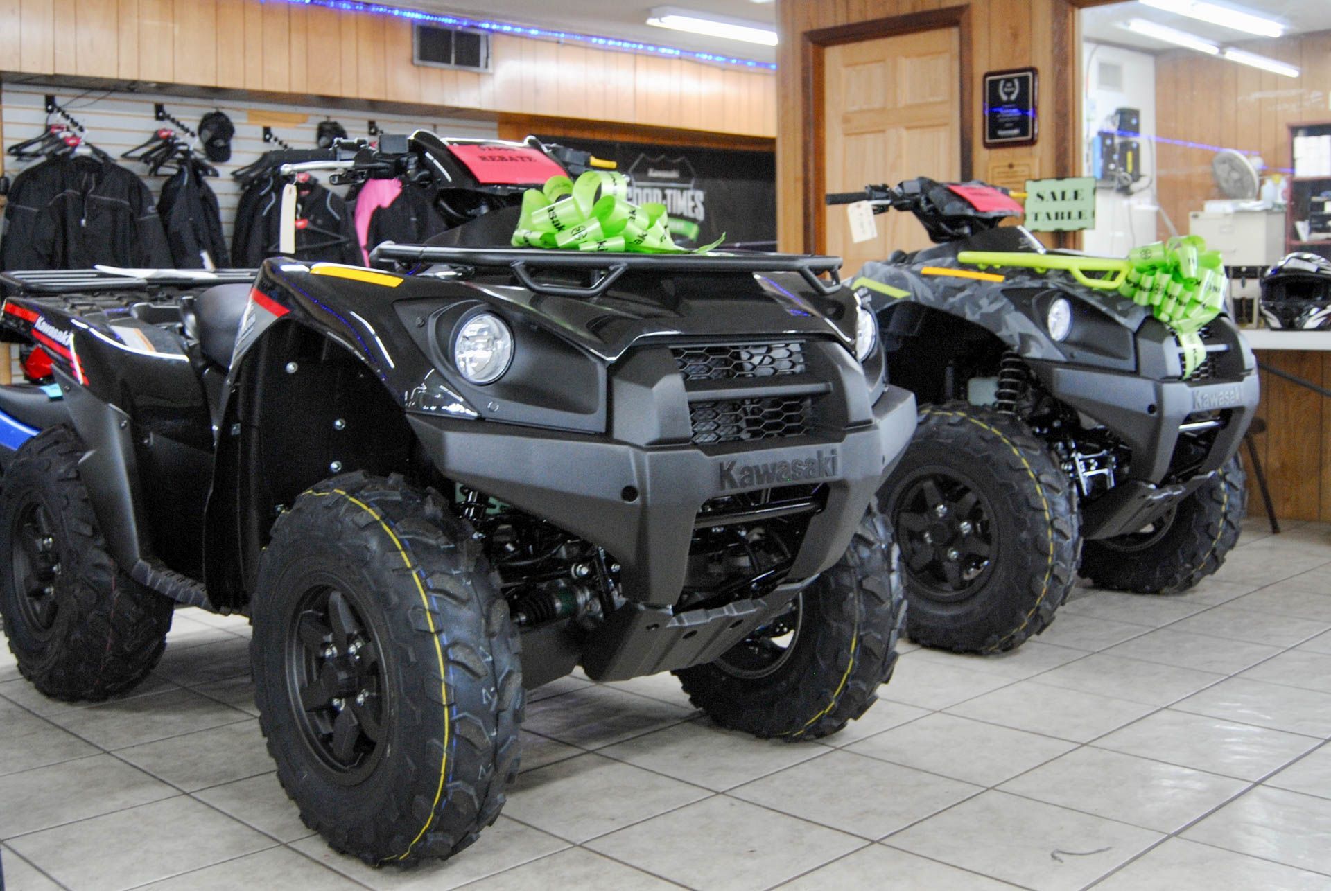 Three kawasaki atvs are parked in a showroom.