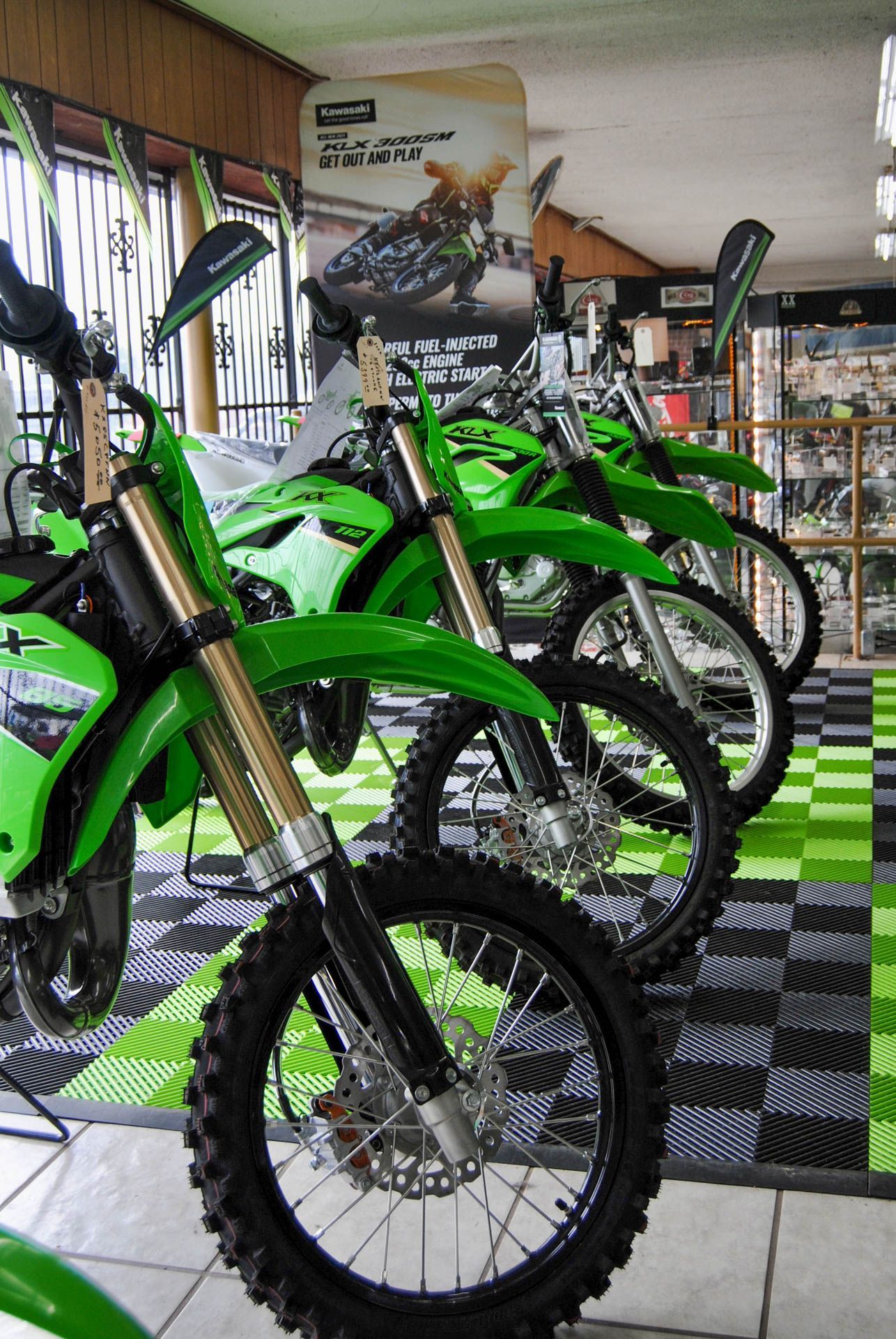 A row of green dirt bikes are lined up in a showroom