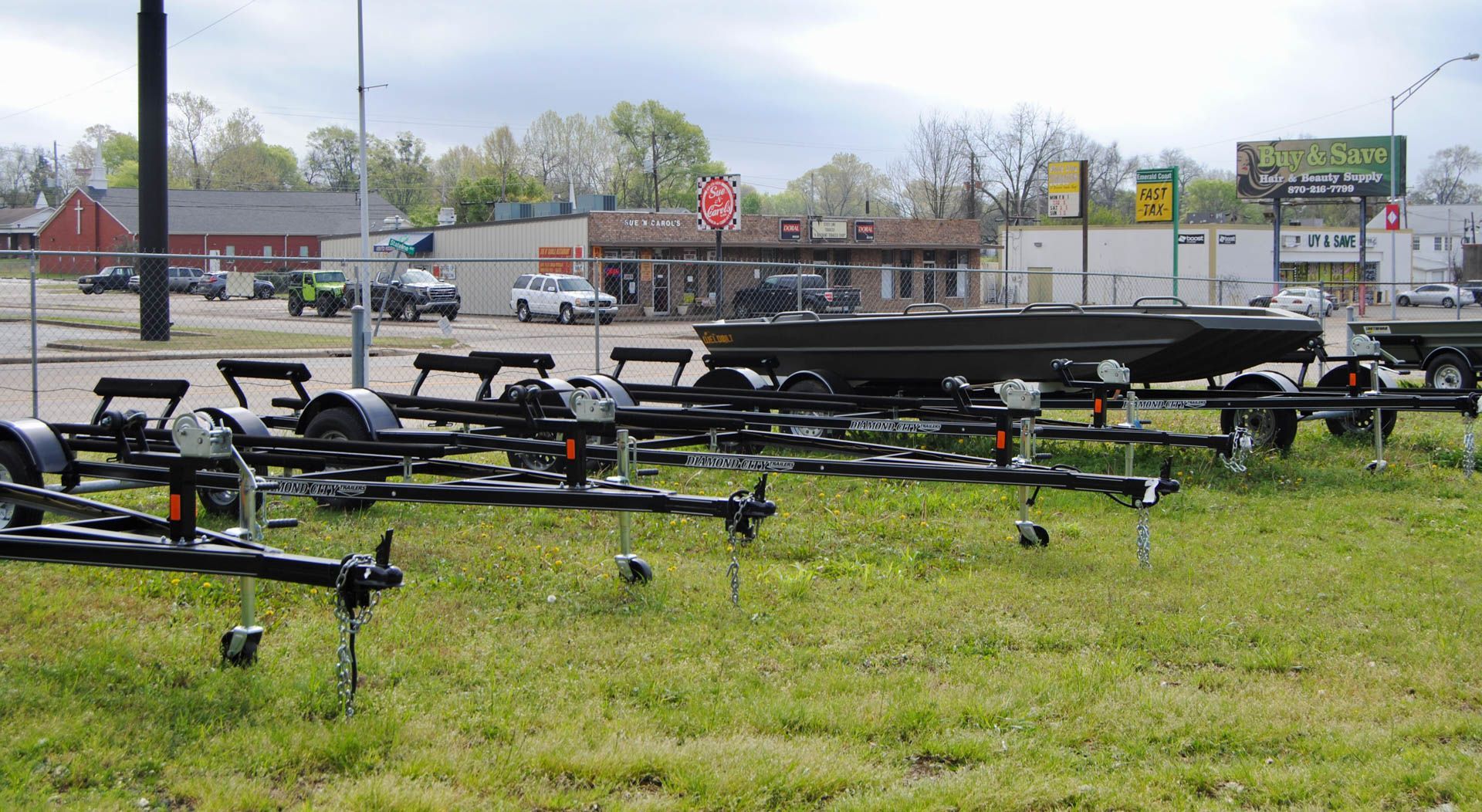 A row of boat trailers are parked in a grassy field.