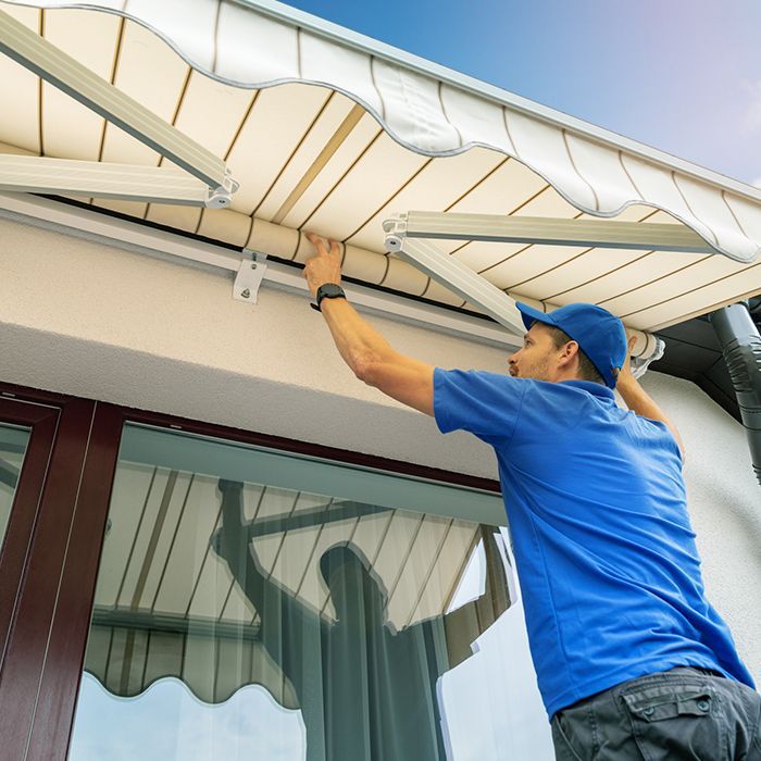 A man in a blue shirt is installing an awning on the side of a building.