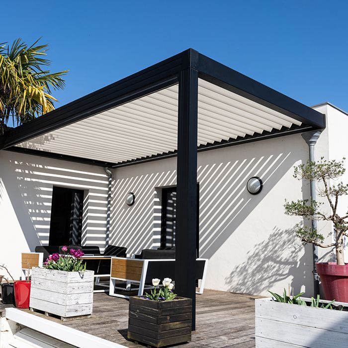 A white house with a black pergola over a wooden deck.