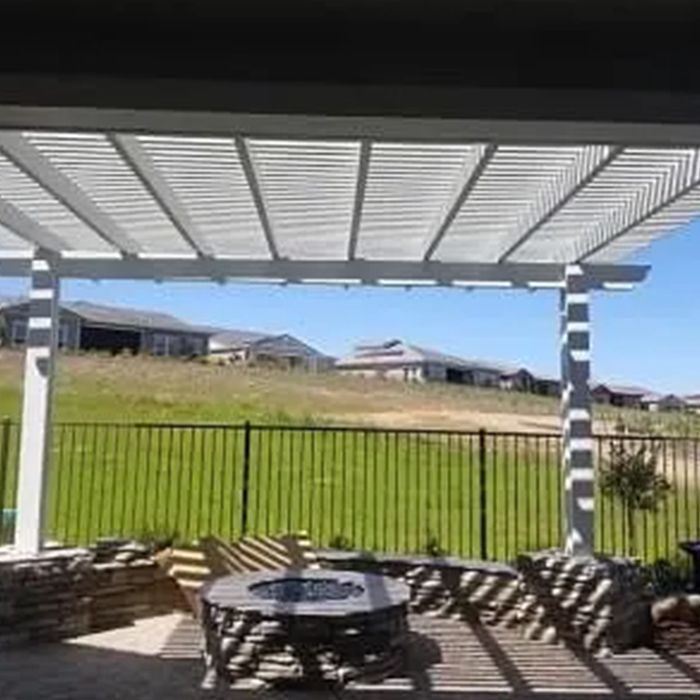 A pergola over a patio with a table and chairs and a fire pit.