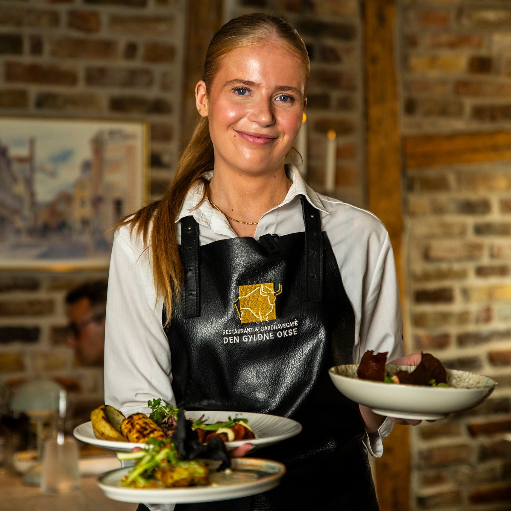 Servitrice smiler og holder to tallerkener mad i en restaurant.