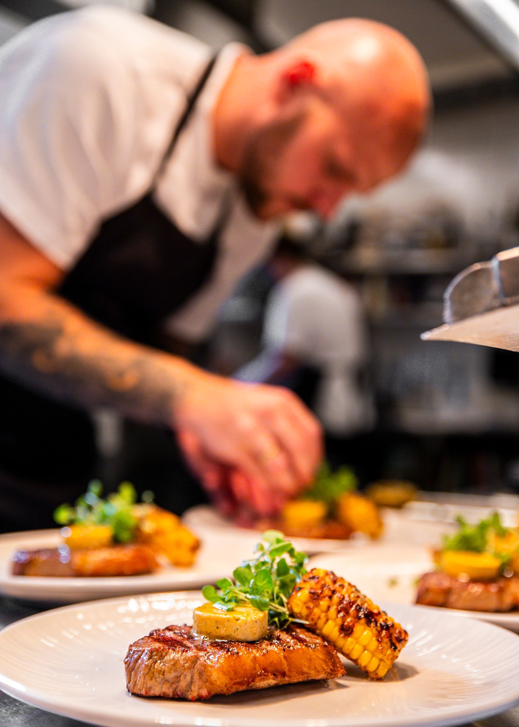 Kokken anretter en ret: grillet bøf, grillet majs og grøntsager. Køkkenindstilling.