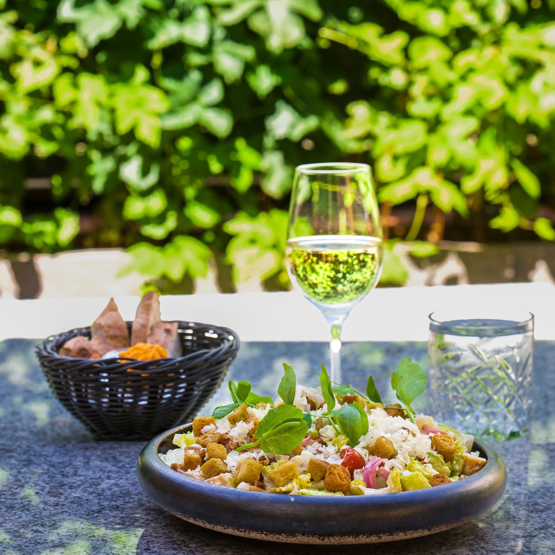 Couscoussalat med vin og vandglas på et bord mod en baggrund af grønne blade.