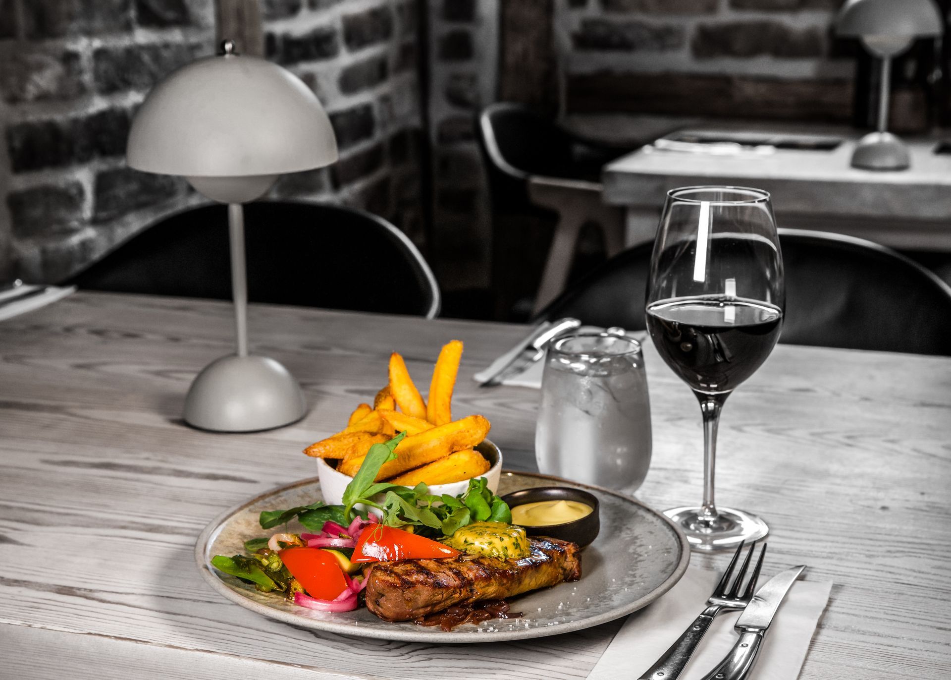 Bøfmiddag med pommes frites, grøntsager, vin og en lampe på et træbord i en restaurant.