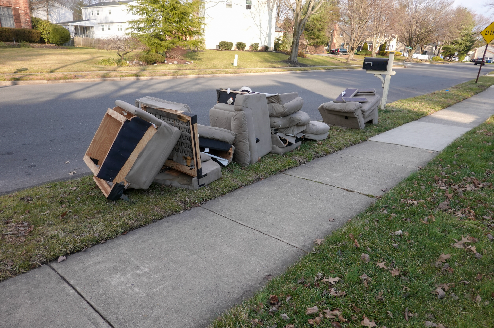 Pile of discarded furniture on the grassy curb next to a sidewalk and street in a residential area.