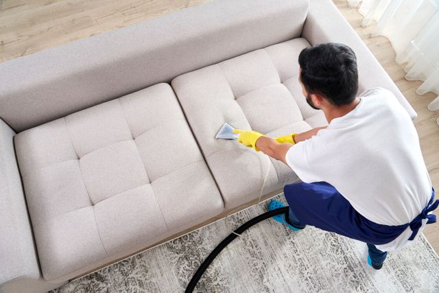 a man is cleaning a couch with a vacuum cleaner .