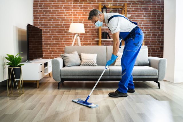 A man wearing a mask is mopping the floor in a living room.