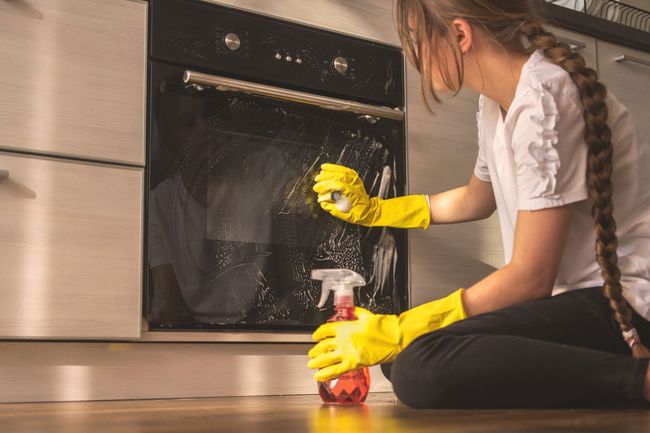 a woman in yellow gloves is cleaning an oven in a kitchen .