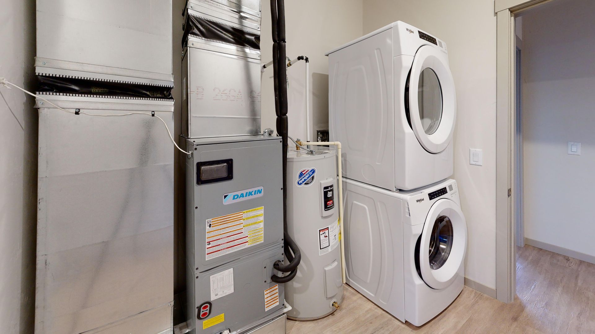 Laundry room with stacked white washer and dryer beside a gray utility panel.