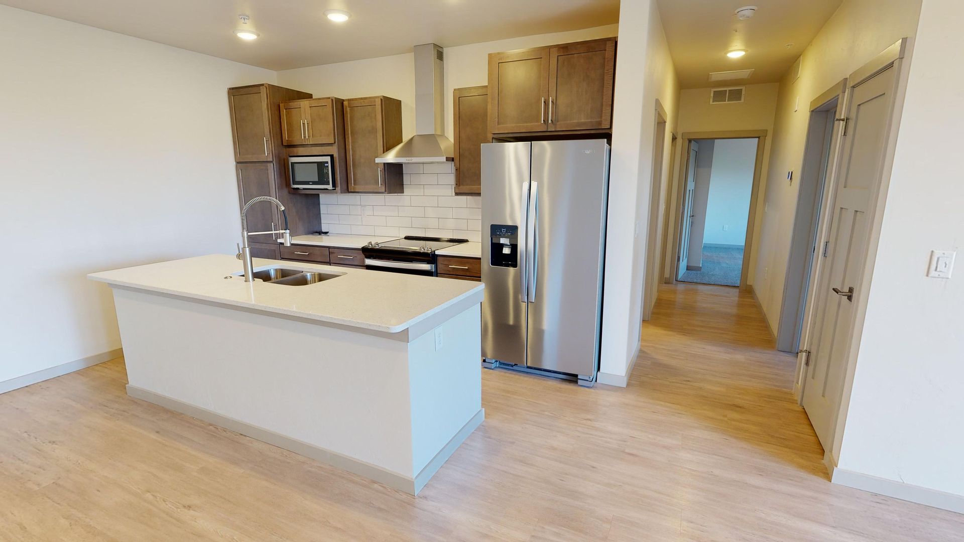 Bright open kitchen with white island, wood cabinets, stainless appliances, and light wood floors