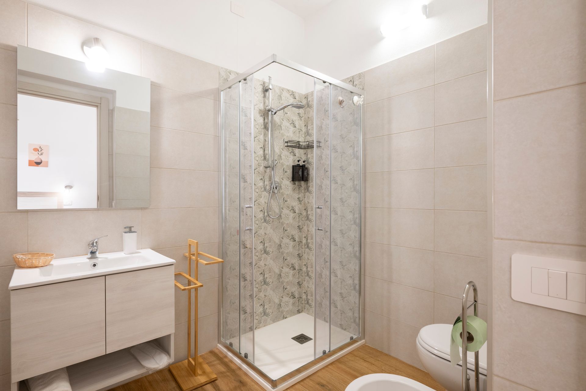 Un bagno moderno dai toni neutri con box doccia in vetro, mobiletto con lavabo, bidet e WC.