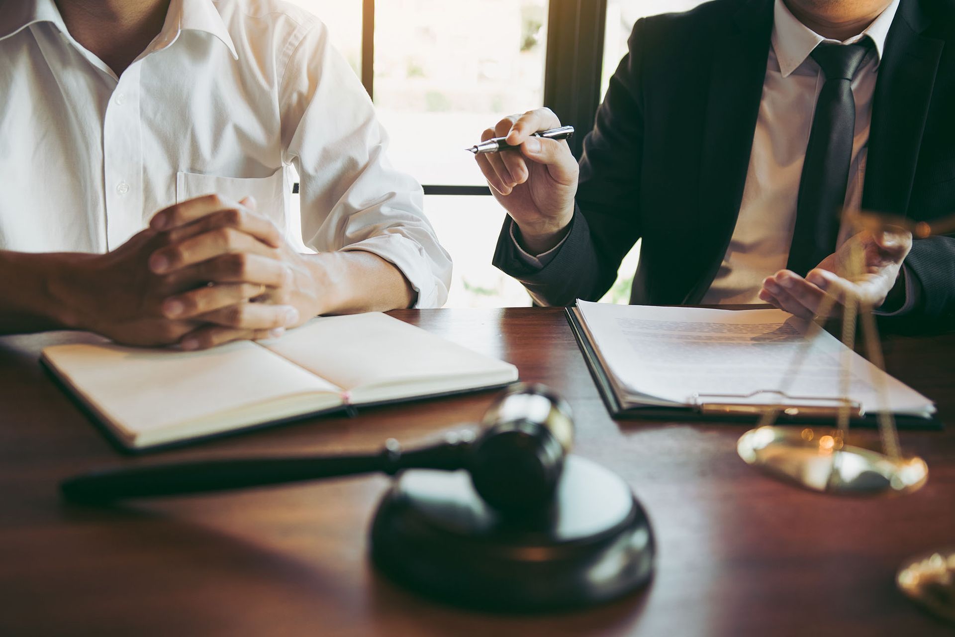 Two professionals sit at a desk with an open document and a judge's gavel, in a legal or business setting.