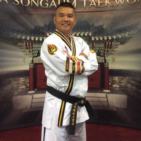 A man in a taekwondo uniform is posing for a picture