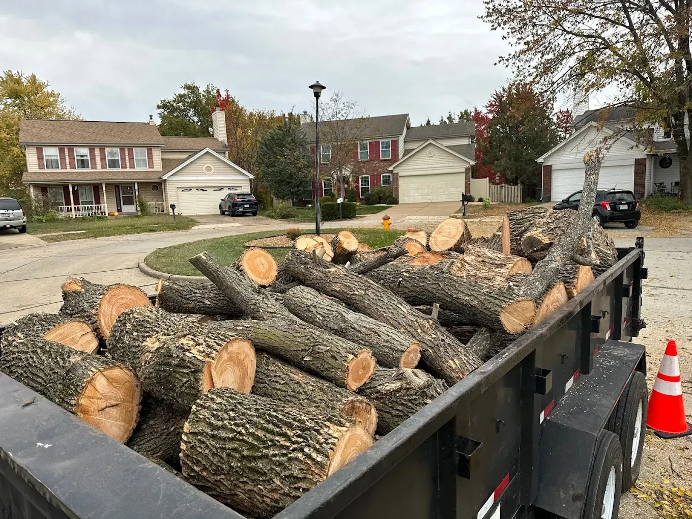 A trailer filled with logs is parked in front of a house.