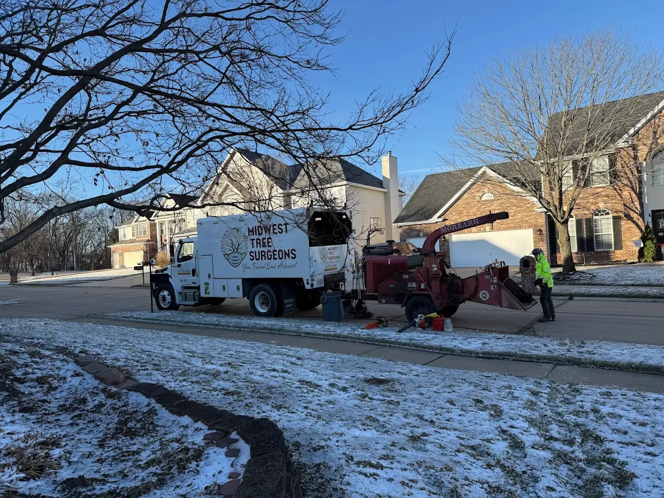 A tree chipper is parked on the side of the road in front of a house.