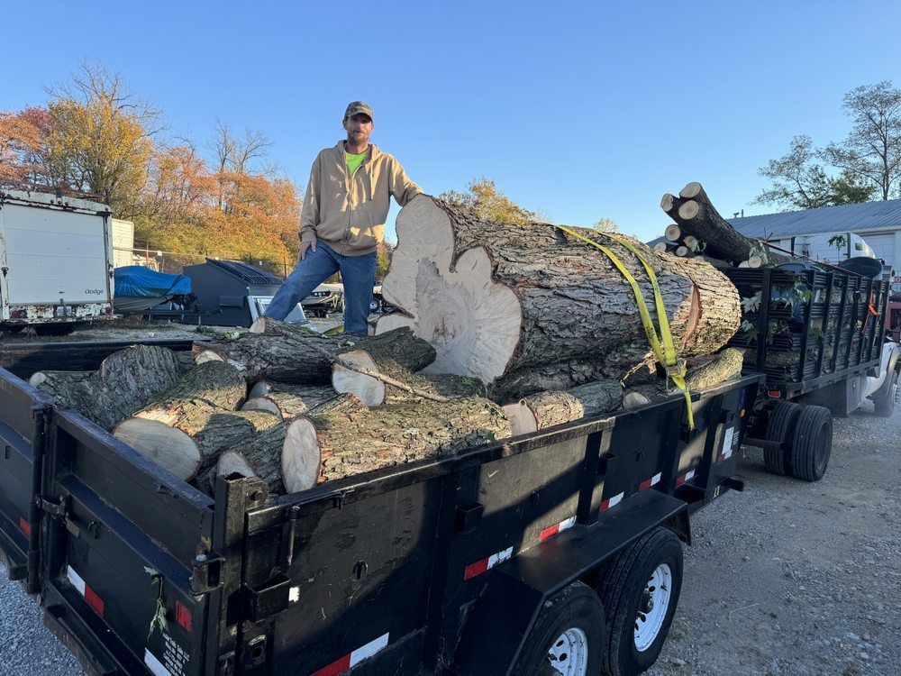 A man is standing next to a trailer filled with logs.
