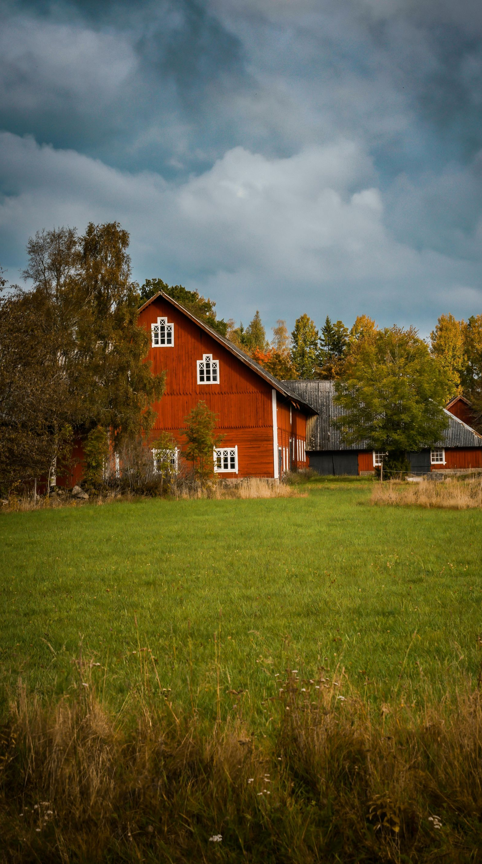 Red barn in a green field under a cloudy sky with trees, possibly autumn.