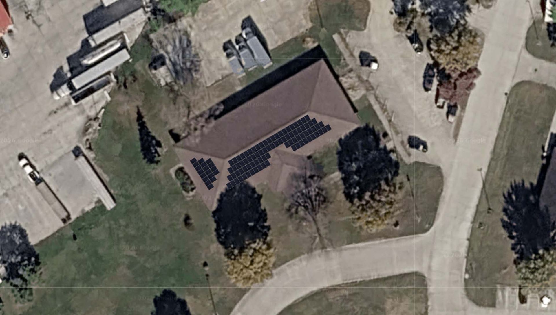 Aerial view of a house with solar panels, surrounded by trees, lawn, and a curving driveway.