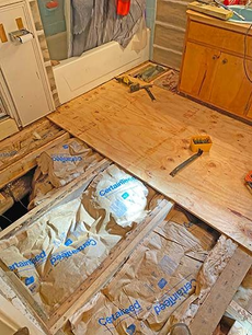 Bathroom remodel: plywood flooring installed over exposed joists, insulation visible.  Yellow cabinet, tools present.