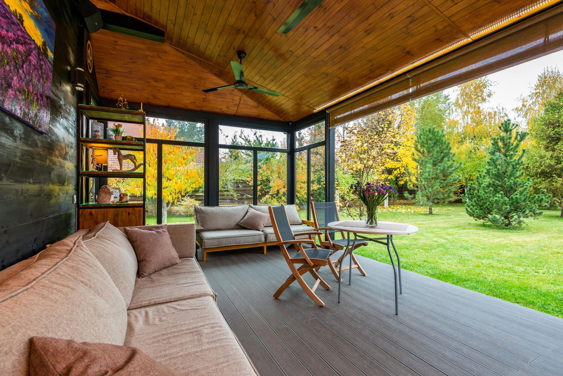 Covered patio with seating overlooking a green lawn and trees; sunlight, neutral colors.