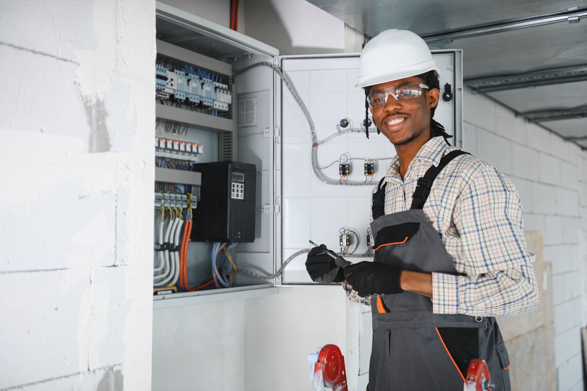 Licensed electrician in safety gear inspecting a commercial electrical panel with all wiring exposed